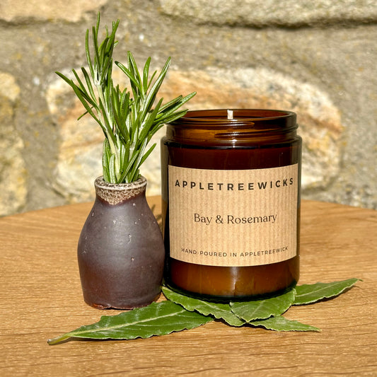 Brown glass jar with bay & rosemary candle surrounded by fresh bay & rosemary