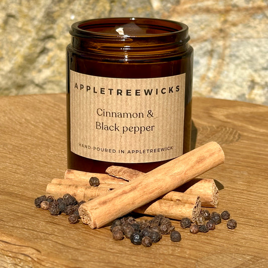 Brown glass jar with cinnamon & black pepper candle and cinnamon sticks & peppercorns next to it