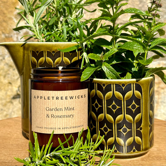 Brown glass jar with garden mint & rosemary candle, surrounded by fresh mint & rosemary in vintage hornsea pottery jugs